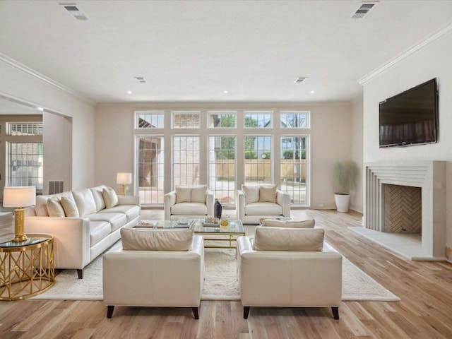 living room with visible vents, light wood-style floors, a fireplace with raised hearth, and crown molding