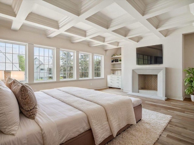 bedroom with baseboards, light wood-style flooring, a fireplace with raised hearth, ornamental molding, and beamed ceiling