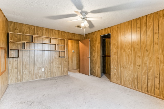 carpeted spare room featuring a textured ceiling, ceiling fan, and wood walls