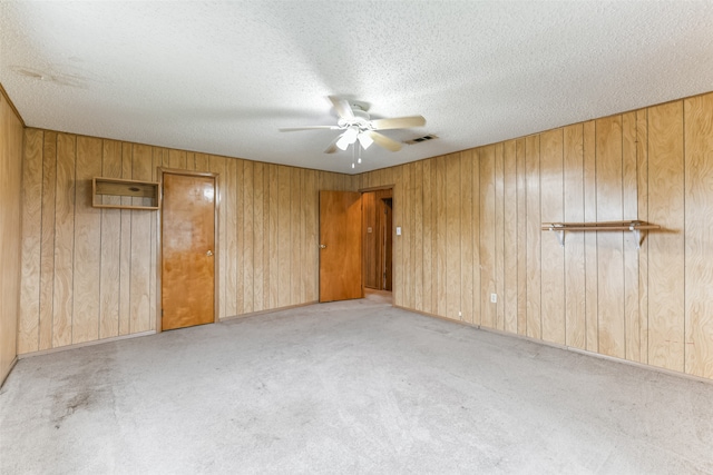 carpeted empty room featuring a textured ceiling, wooden walls, and ceiling fan