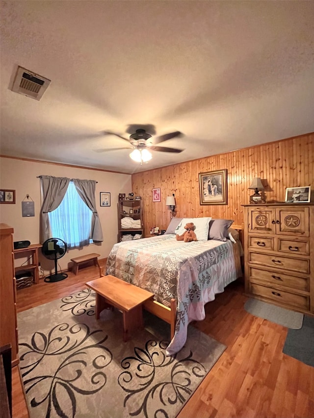 bedroom with wooden walls, ceiling fan, and light wood-type flooring