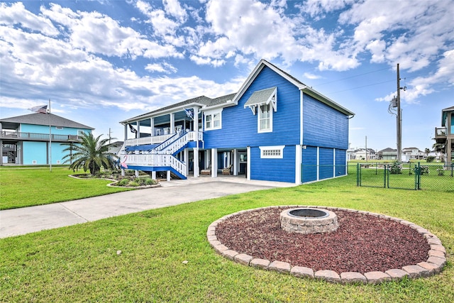 coastal inspired home with a wooden deck, a fire pit, a front lawn, and a patio