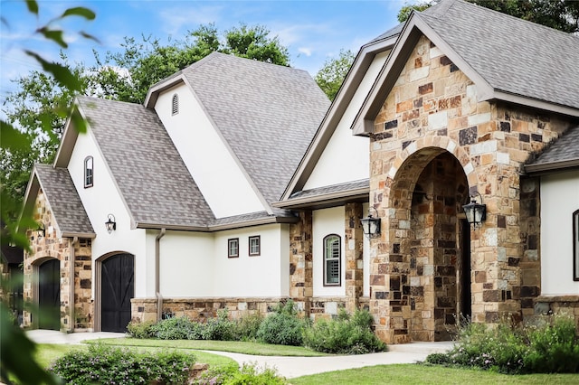 view of front of house with stone siding, roof with shingles, and stucco siding