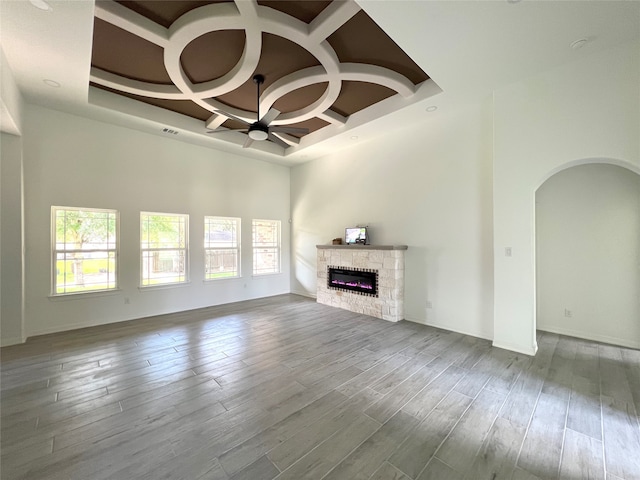 unfurnished living room with coffered ceiling, hardwood / wood-style floors, beamed ceiling, a fireplace, and a chandelier