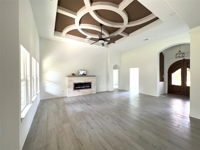 unfurnished living room featuring hardwood / wood-style floors, a stone fireplace, ceiling fan, and coffered ceiling