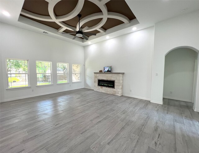 unfurnished living room with coffered ceiling, a fireplace, light hardwood / wood-style floors, a towering ceiling, and a chandelier