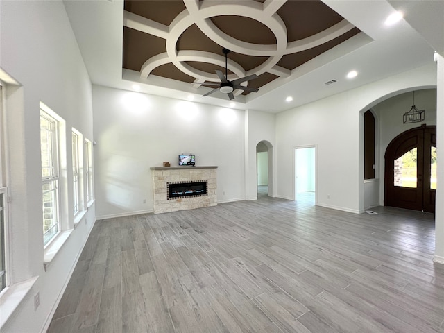 unfurnished living room featuring coffered ceiling, ceiling fan, a fireplace, light hardwood / wood-style flooring, and a towering ceiling