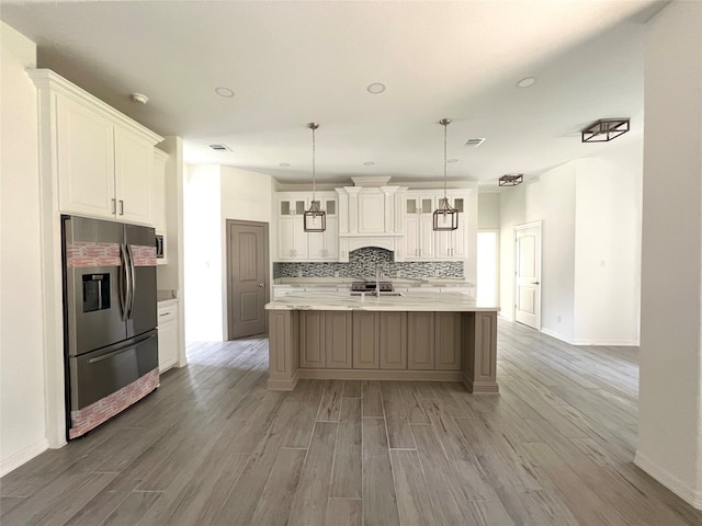 kitchen featuring tasteful backsplash, white cabinets, an island with sink, stainless steel refrigerator with ice dispenser, and hanging light fixtures