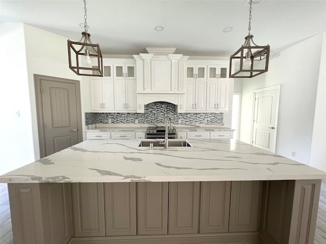 kitchen featuring white cabinets, decorative light fixtures, sink, and a kitchen island with sink