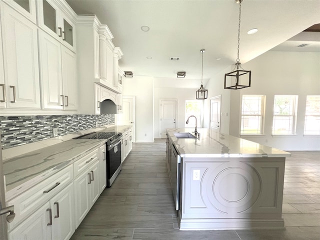 kitchen featuring white cabinets, pendant lighting, light stone countertops, and an island with sink