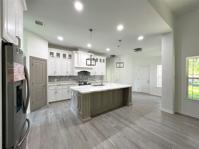 kitchen featuring light hardwood / wood-style floors, stainless steel appliances, tasteful backsplash, white cabinets, and a kitchen island with sink