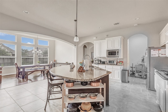 kitchen with appliances with stainless steel finishes, an island with sink, light tile floors, white cabinets, and light stone counters