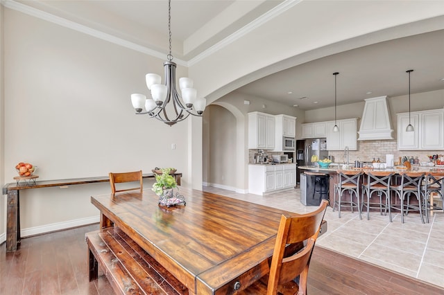 dining area with an inviting chandelier, sink, a raised ceiling, and light tile floors