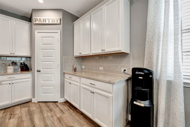 kitchen featuring white cabinetry, light stone countertops, light hardwood / wood-style floors, and decorative backsplash