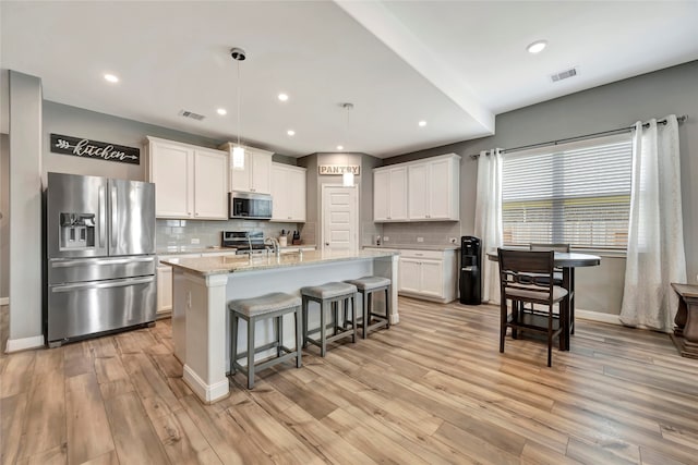 kitchen featuring appliances with stainless steel finishes, pendant lighting, white cabinetry, an island with sink, and light stone countertops