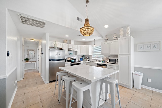 kitchen featuring a kitchen island, a kitchen breakfast bar, hanging light fixtures, stainless steel appliances, and white cabinetry