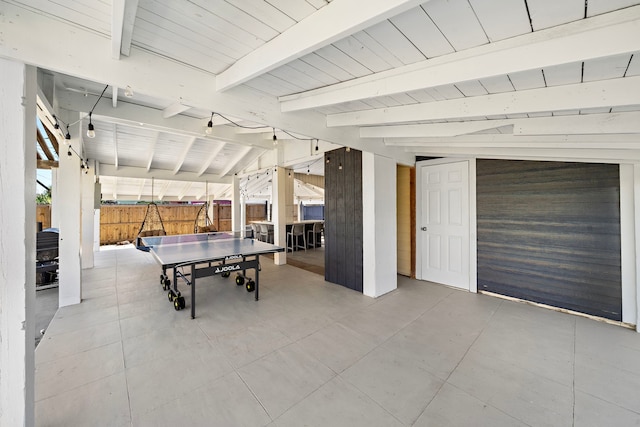 recreation room with wooden walls, light tile flooring, and lofted ceiling with beams