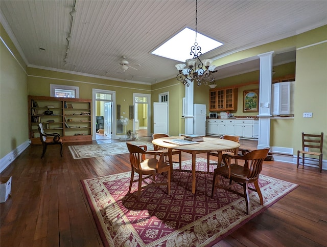 dining room with rail lighting, ceiling fan with notable chandelier, dark wood-type flooring, crown molding, and ornate columns