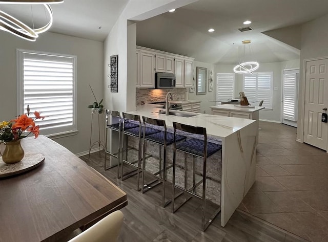 kitchen featuring backsplash, dark tile flooring, decorative light fixtures, sink, and white cabinetry