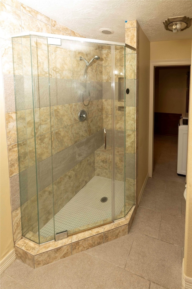 bathroom featuring washer / clothes dryer, a textured ceiling, tile flooring, and an enclosed shower