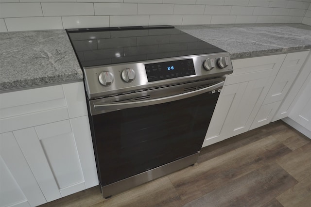 kitchen featuring stainless steel electric range, dark hardwood / wood-style flooring, white cabinets, light stone countertops, and backsplash