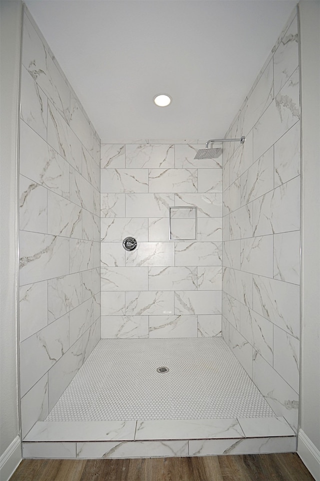 bathroom with a tile shower and wood-type flooring