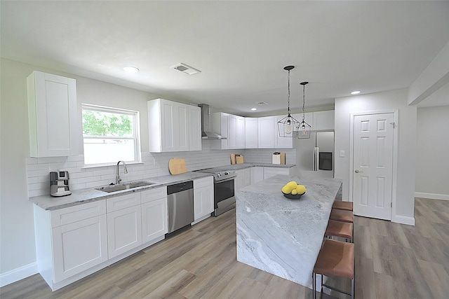 kitchen with stainless steel appliances, light hardwood / wood-style flooring, sink, and wall chimney range hood