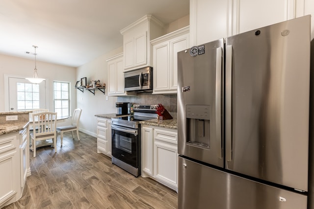 kitchen featuring light stone counters, white cabinetry, stainless steel appliances, backsplash, and hanging light fixtures