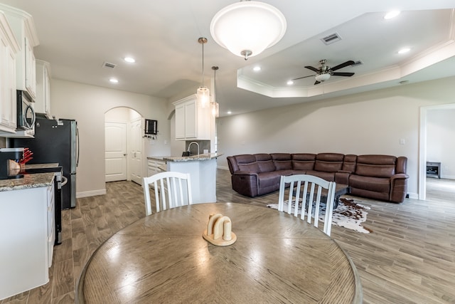 dining space featuring light hardwood / wood-style flooring, ceiling fan, a raised ceiling, and sink