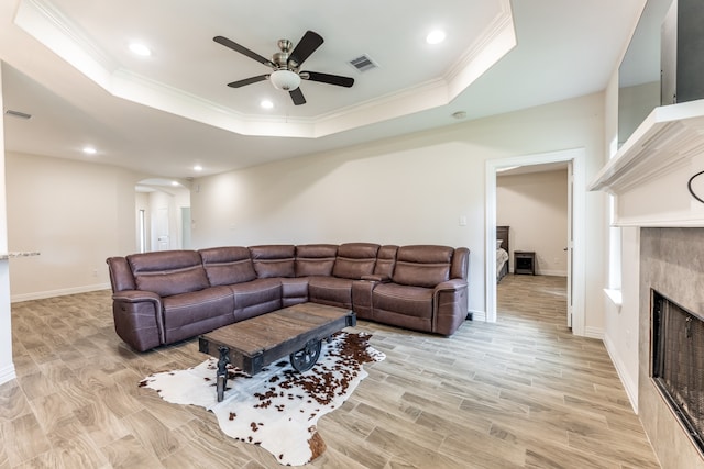 living room featuring a tiled fireplace, ceiling fan, crown molding, and a raised ceiling