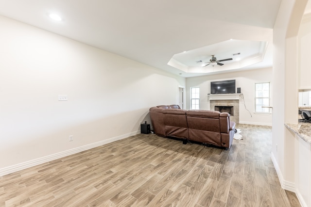 living room featuring a raised ceiling, ceiling fan, and light wood-type flooring