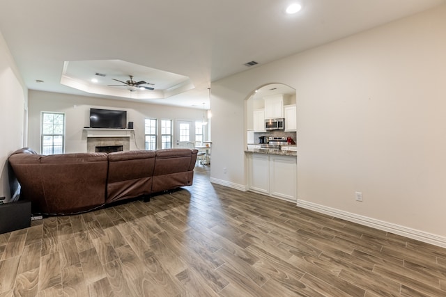 living room with ceiling fan, wood-type flooring, and a raised ceiling