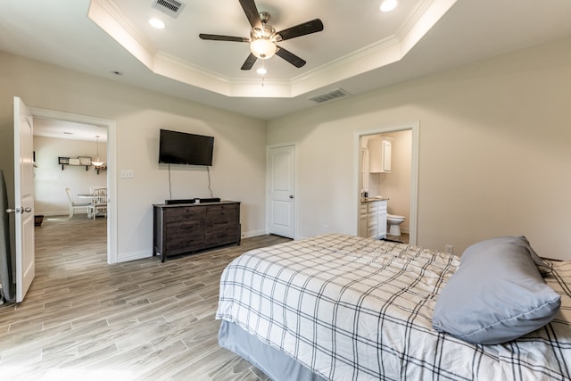 bedroom featuring ensuite bath, a tray ceiling, light hardwood / wood-style floors, and ceiling fan