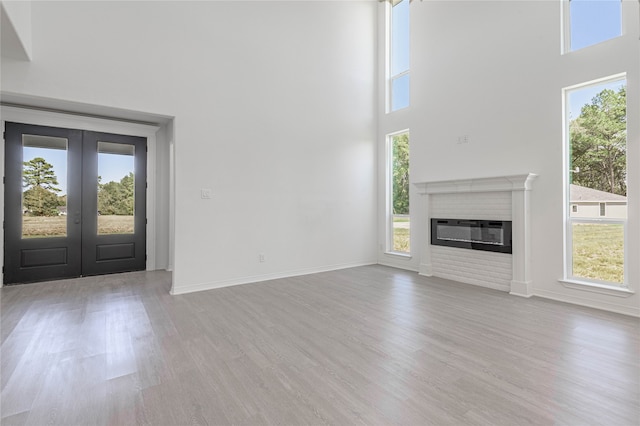 unfurnished living room featuring a brick fireplace, plenty of natural light, french doors, and light wood-type flooring