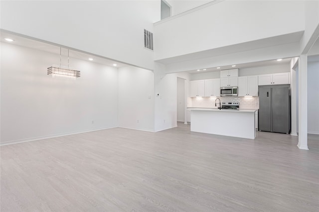 unfurnished living room with sink, light hardwood / wood-style floors, and a towering ceiling