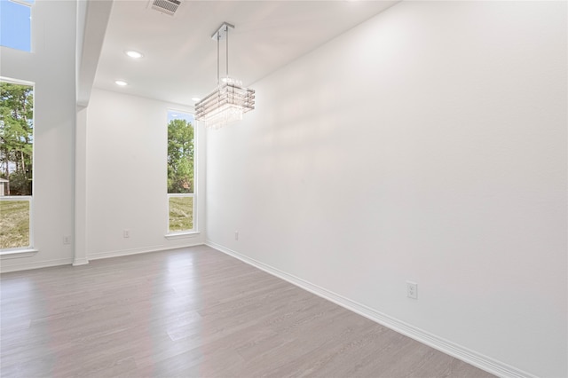 empty room with an inviting chandelier, wood-type flooring, and a healthy amount of sunlight