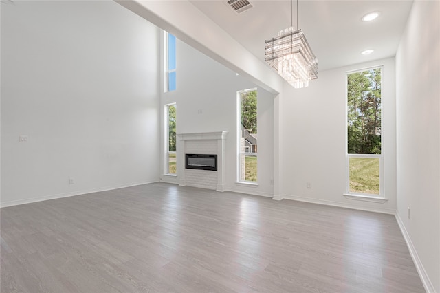 unfurnished living room with a towering ceiling, a notable chandelier, and light wood-type flooring