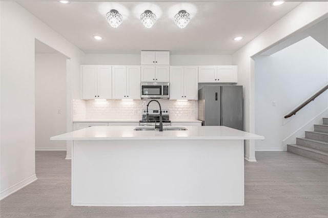 kitchen featuring white cabinetry, appliances with stainless steel finishes, light hardwood / wood-style floors, and a kitchen island with sink