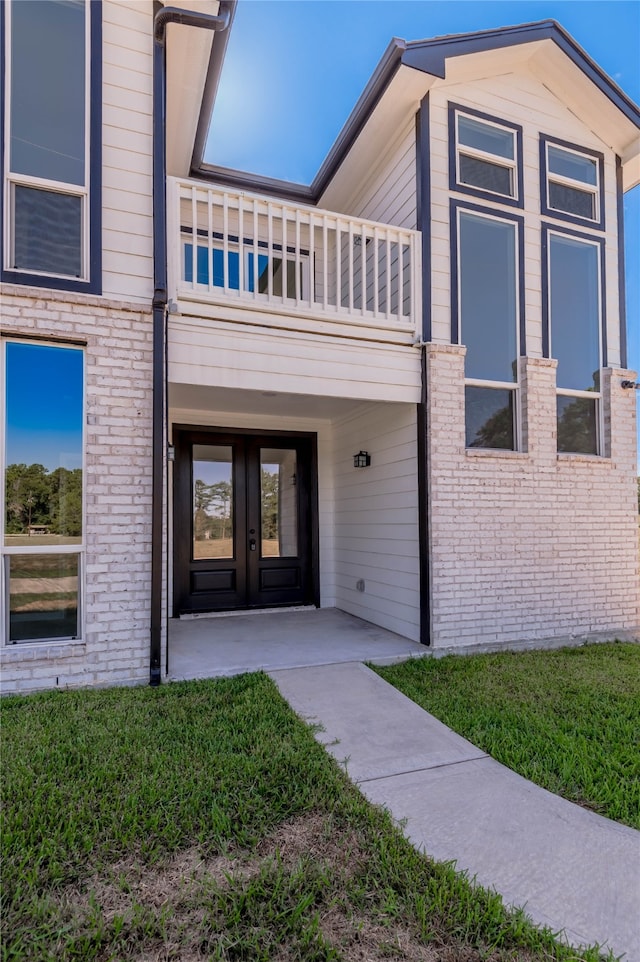 entrance to property featuring a balcony, a lawn, a patio area, and french doors