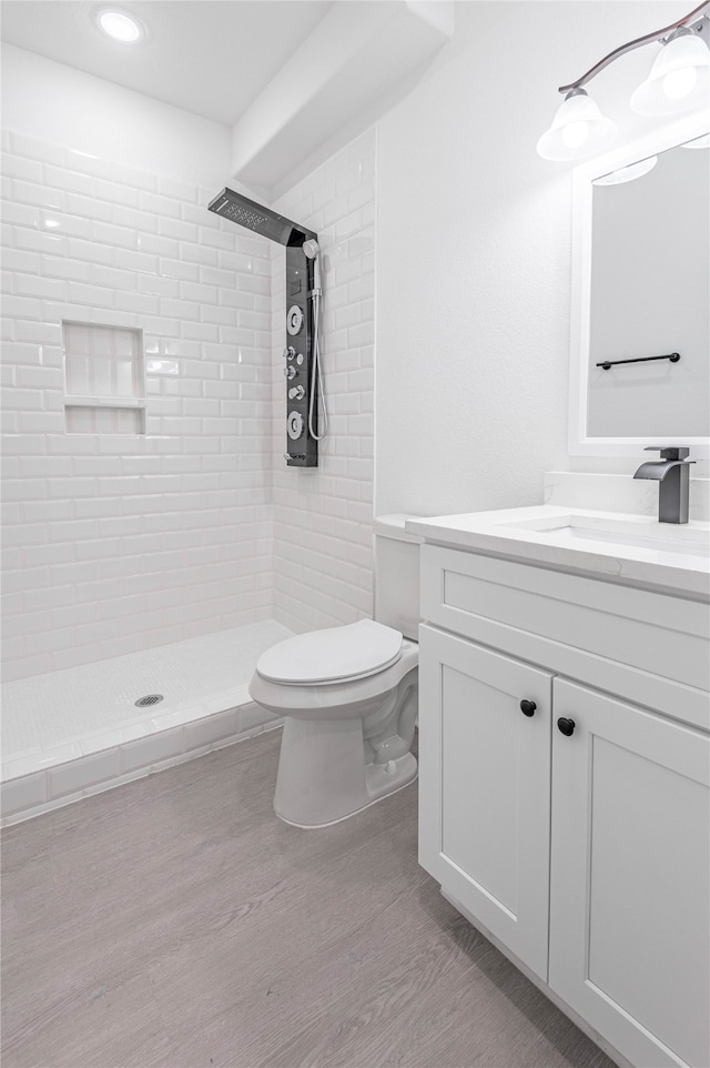 bathroom with wood-type flooring, a tile shower, vanity, and toilet