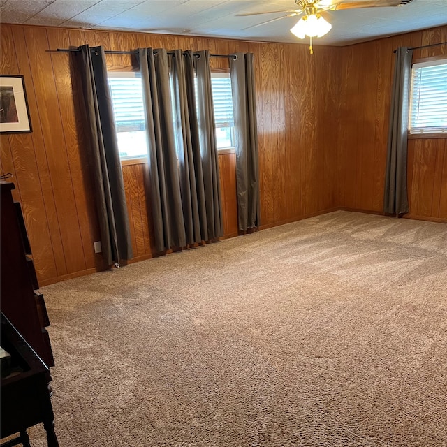 carpeted spare room featuring plenty of natural light, wooden walls, and ceiling fan