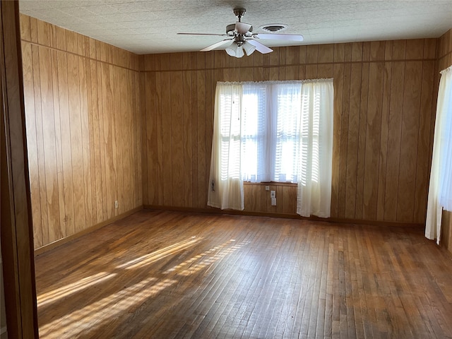 empty room featuring wooden walls, ceiling fan, and dark hardwood / wood-style floors
