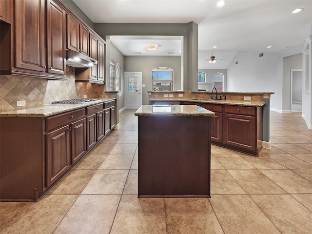 kitchen with stainless steel gas cooktop, light stone counters, dark brown cabinets, a kitchen island, and decorative backsplash