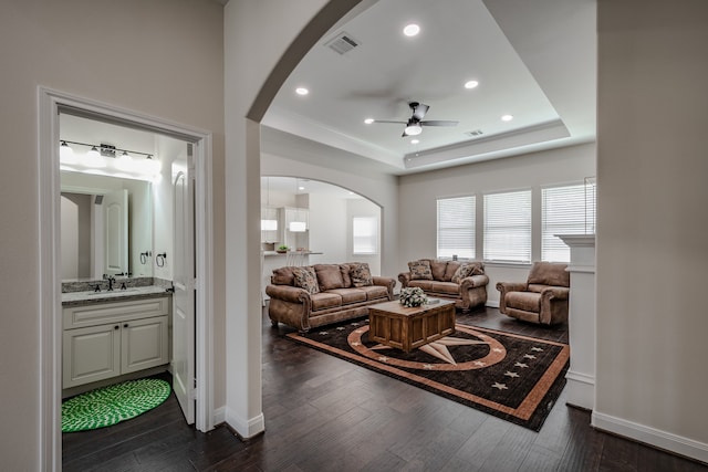 living room featuring dark hardwood / wood-style flooring, ceiling fan, sink, and a raised ceiling