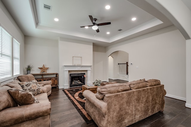 living room featuring a raised ceiling, ceiling fan, and dark wood-type flooring