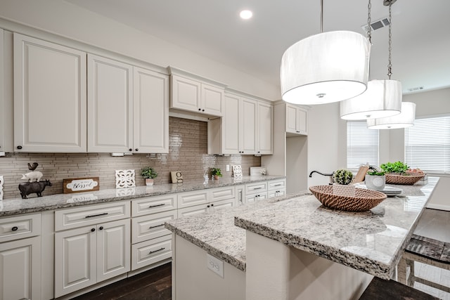 kitchen with white cabinets, backsplash, pendant lighting, and light stone countertops