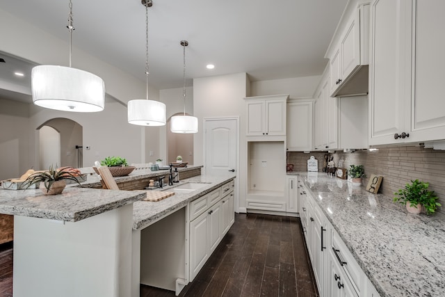 kitchen featuring decorative light fixtures, white cabinetry, dark wood-type flooring, a center island with sink, and tasteful backsplash