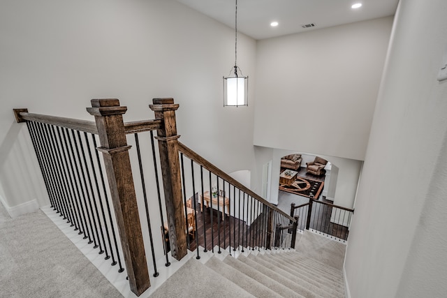 stairway with a towering ceiling and light colored carpet