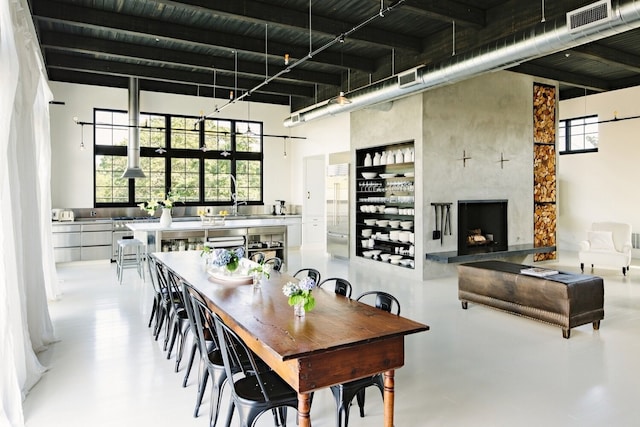 dining area with a wealth of natural light, finished concrete floors, a towering ceiling, and a premium fireplace