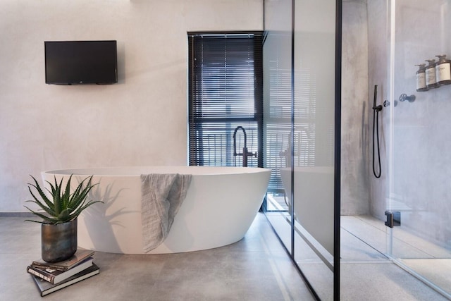 bathroom with a soaking tub, walk in shower, and finished concrete flooring